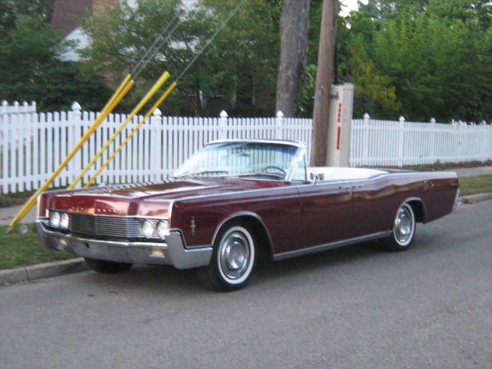 Maroon convertible parked on street, white fence behind it