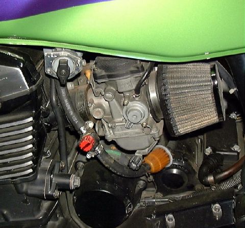 1999 Kawasaki H2C - Close-up view of a motorcycle's engine components, including the carburetor and air filter, with a portion of the green fuel tank visible.
