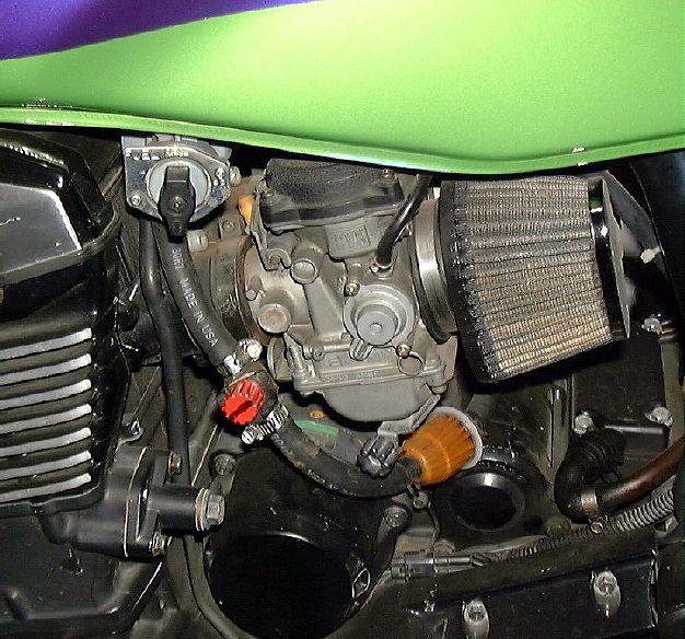 Motorcycle carburetor with mesh pod filter and red inline fuel valve under a green and purple tank
