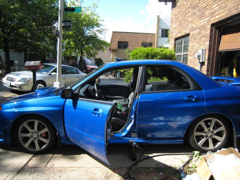 2007 Subaru Impreza - A blue Subaru Impreza sedan is parked outside a garage with its doors open, showing the interior.
