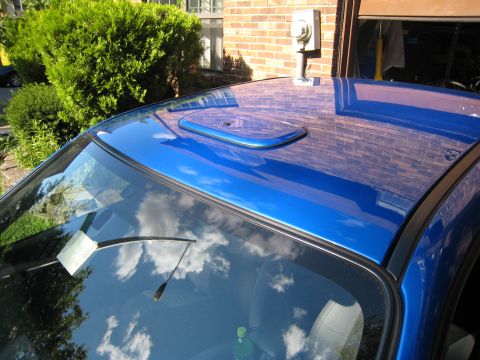 2007 Subaru Impreza - A close-up view of a blue car's roof, a vent and reflections of the sky and a brick building.