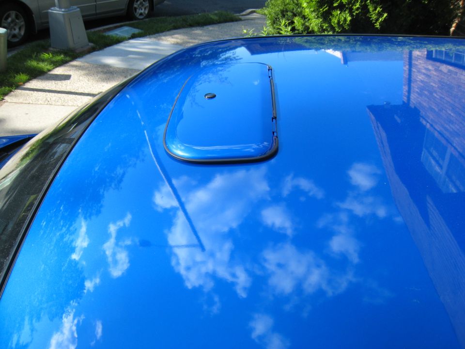 Blue car roof with body-color sunroof tilted open in vent position, sky reflected in paint
