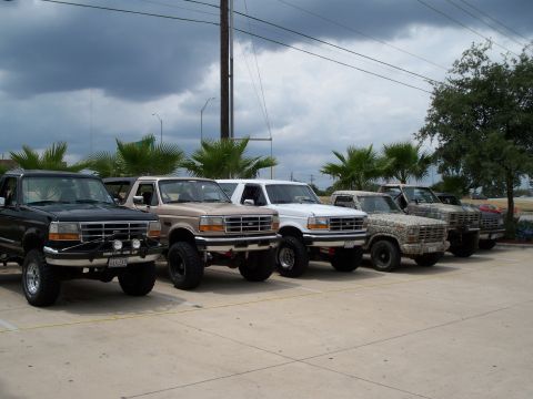 1996 Ford Bronco - A row of Ford Bronco SUVs, including a black, tan, white, and camouflage-painted model.