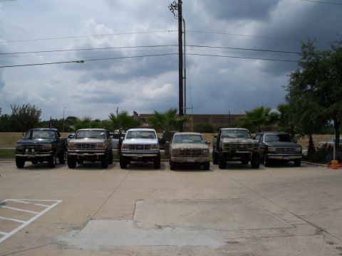 1996 Ford Bronco - A lineup of Ford F-Series trucks from the early to mid-1990s are parked in a lot under a cloudy sky.