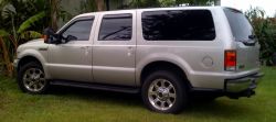 2005 Ford Excursion - This 2005 Ford Excursion is seen from the rear three-quarter angle, parked on grass with foliage in the background.