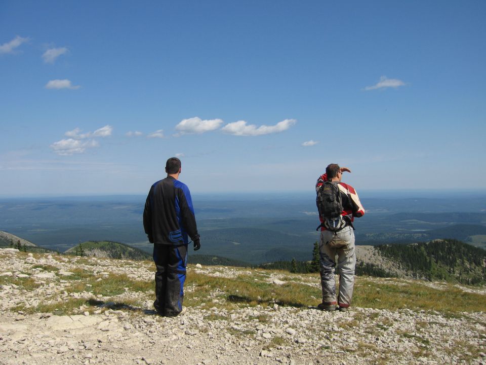 Two men on a hilltop, one pointing towards the horizon, with a wide landscape below