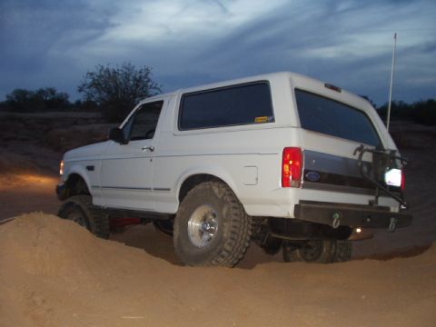1992 Ford Bronco - White 1992 Ford Bronco navigates sandy terrain, its off-road capability.
