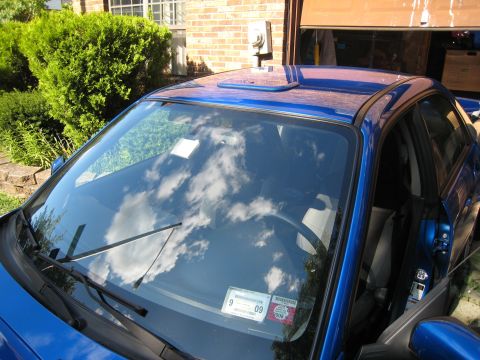 2007 Subaru Impreza - A blue car with a roof vent is parked in front of a garage, showing a 2009 inspection sticker on the windshield.