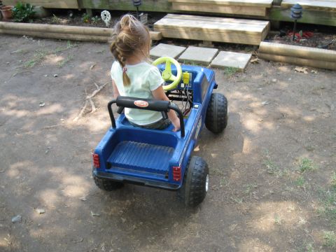 1994 Ford Bronco - A child sits in a blue toy truck, steering it from the driver's seat.