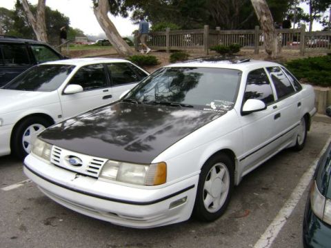 1991 Ford Taurus - A white 1991 Ford Taurus sedan with a contrasting black hood is parked outdoors.