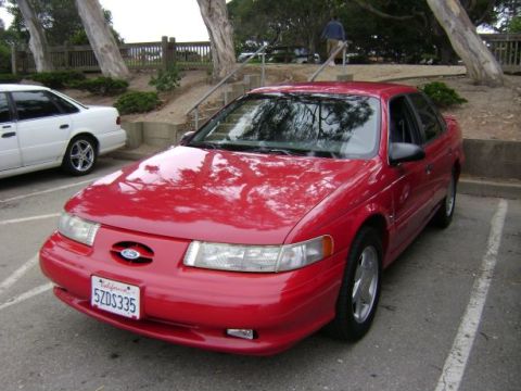 1991 Ford Taurus - A red 1991 Ford Taurus is parked in a lot, with another white vehicle nearby.