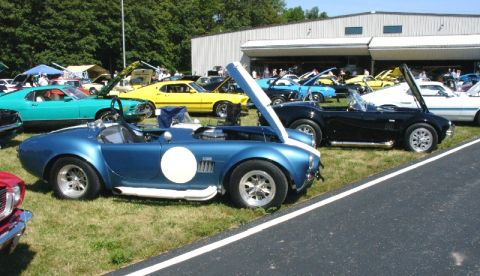 2003 Ford Crown Victoria - Several classic cars are on display at an outdoor event, with a focus on two Shelby Cobra replicas.