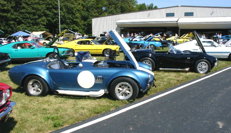 Blue Shelby Cobra replica roadster with white roundel at an outdoor car show