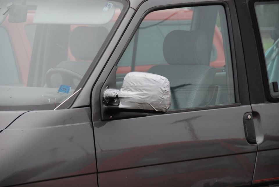 Gray van side mirror covered in silver duct tape. Another vehicle is visible in the background