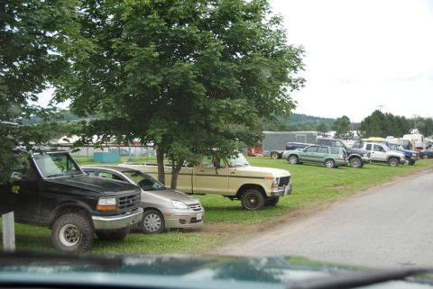 1996 Ford Bronco - Several vehicles are parked on a grassy area next to a road under trees.