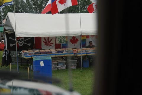 1996 Ford Bronco - An outdoor market stall displays various flags, including Canadian flags, a pirate flag, and a flag with a marijuana leaf, with merchandise…