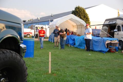 1996 Ford Bronco - Foreground shows a blue truck's fender and tire, with people gathered around tents and vehicles in the background.