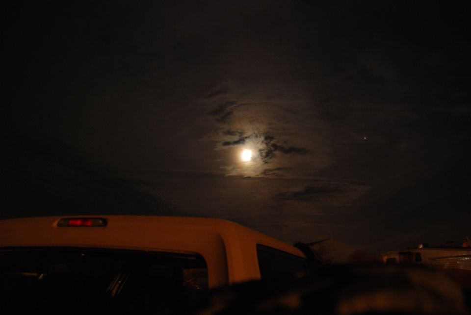 White truck bed with a red brake light under a cloudy night sky with a full moon