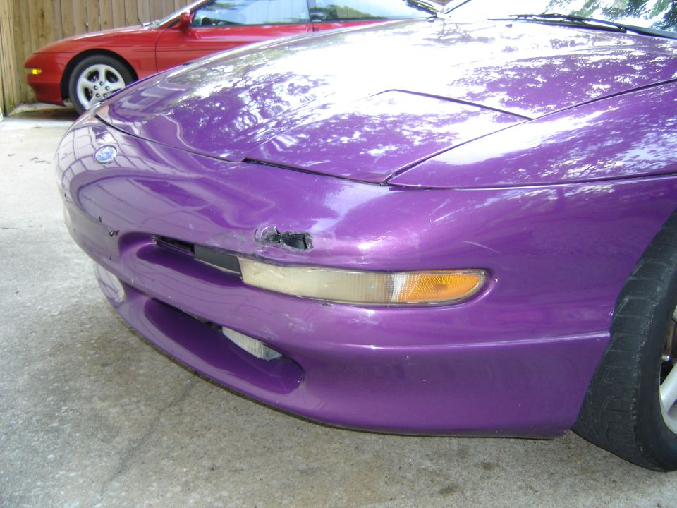 purple car front end with damage on bumper, red car behind it