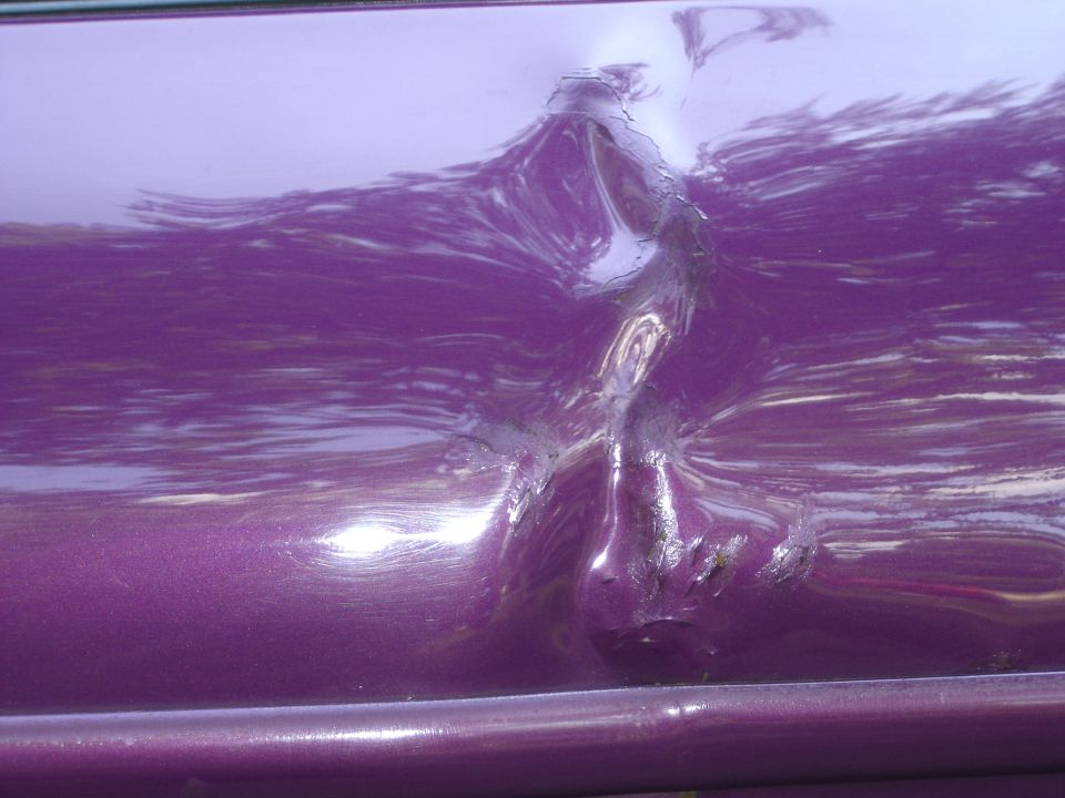 Purple car door with a large dent and scraped paint