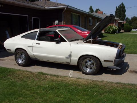 1978 Ford Mustang II - White 1978 Ford Mustang II coupe sits in a driveway with its hood up, a red car visible behind it.