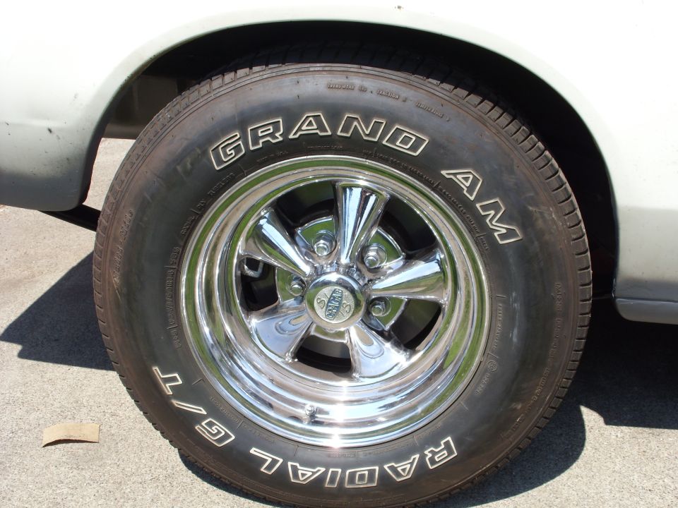Chrome five-spoke wheel with 'GRAND AM' and 'RADIAL G/T' tires on a white car