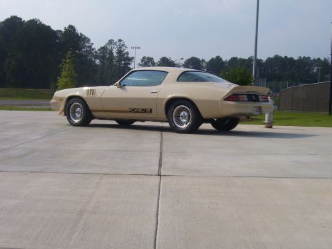 1979 Chevrolet Camaro - This tan Chevrolet Camaro Z28 is parked outside on a paved lot with trees in the background.