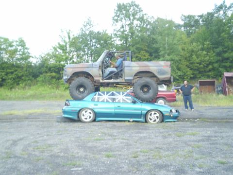 1979 Ford Bronco - A heavily modified truck is parked on top of a sedan, with a person in each vehicle.