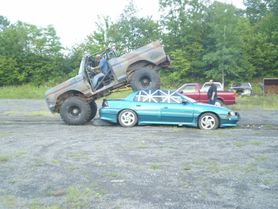 Modified truck on top of a teal sedan with white tape on windows