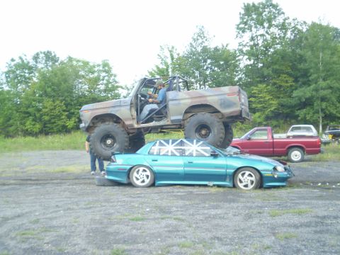 1979 Ford Bronco - A heavily modified 1979 Ford Bronco is parked on top of a sedan, with a red pickup truck in the background.
