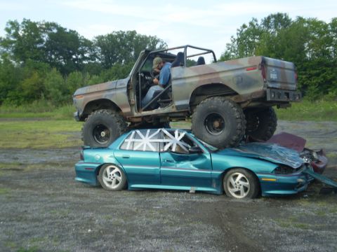 1979 Ford Bronco - A heavily modified truck is crushing a sedan, with a person visible inside the truck's cab.
