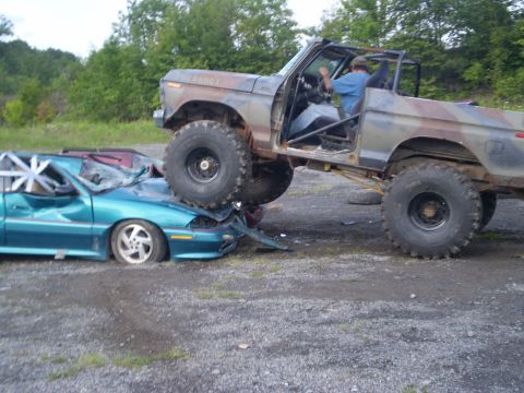 1979 Ford Bronco - A lifted, camouflaged truck is shown crushing a teal sedan.