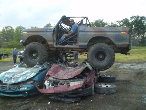 1979 Ford Bronco - A heavily modified truck is positioned atop several wrecked cars, demonstrating its off-road capabilities.