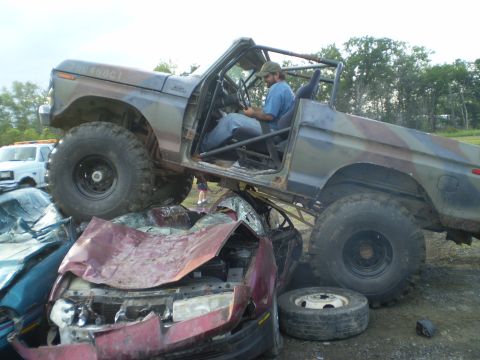 1979 Ford Bronco - A heavily modified off-road vehicle is positioned atop several crushed cars, with a driver inside.