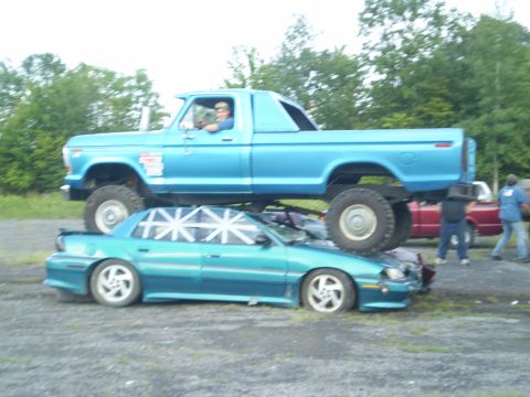1979 Ford Bronco - A blue pickup truck is shown crushing a teal sedan, with the SuperMotors.net logo visible at the bottom right.
