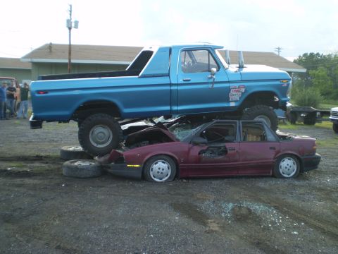 1979 Ford Bronco - A blue 1979 Ford F-Series pickup truck is crushing a red sedan in a junkyard scene.