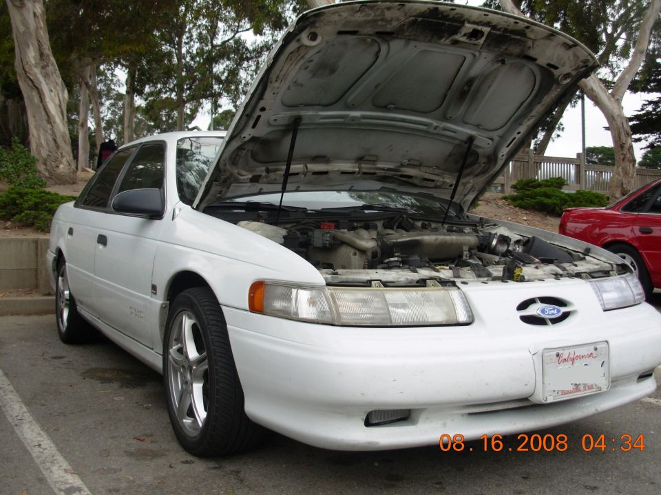 White 1995 Ford Taurus with hood open, parked outside. Another red car is visible to the right