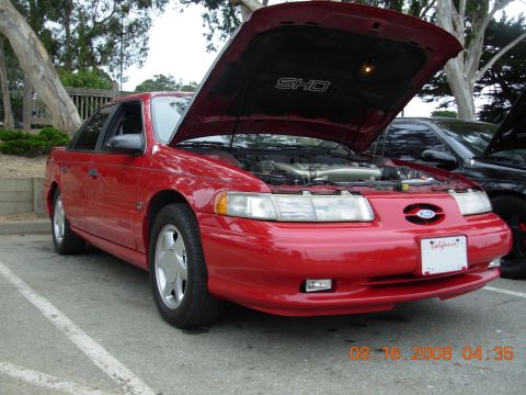 1995 Ford Taurus - A red 1995 Ford Taurus SHO is parked with its hood open, revealing the engine compartment.