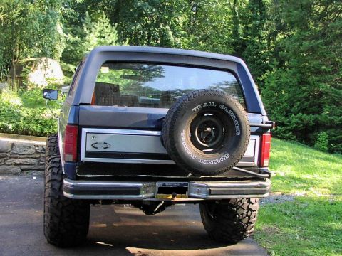 1986 Ford Bronco - Rear view of a lifted Ford Bronco with off-road tires and a spare tire on the tailgate.