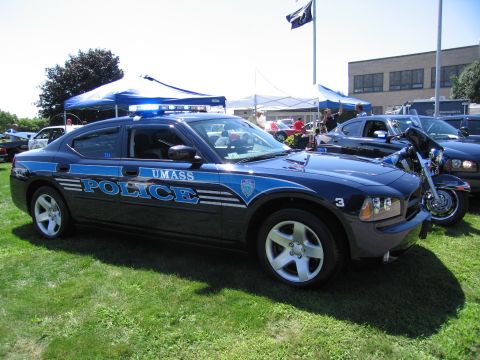 1991 Ford LTD Crown Victoria - Driver-side profile of a dark blue UMass Police Dodge Charger cruiser parked on grass at an outdoor car show.
