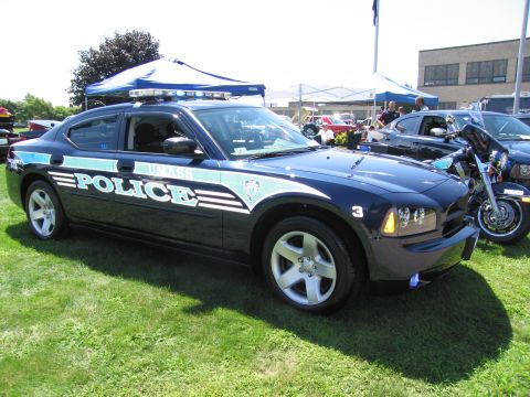 1991 Ford LTD Crown Victoria - Front driver-side view of a dark blue UMass Police Dodge Charger with light bar, on grass near a motorcycle.