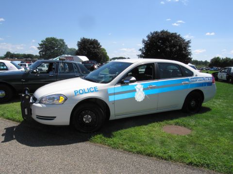 1991 Ford LTD Crown Victoria - Driver-side profile of a white and blue Chevrolet Impala police sedan parked on grass at an outdoor event.