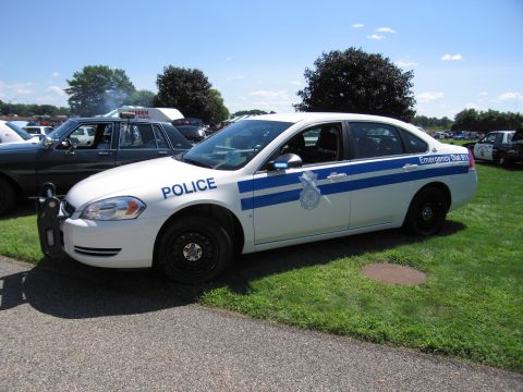 1991 Ford LTD Crown Victoria - white late-2000s Chevrolet Impala police cruiser with a blue stripe and POLICE lettering parked on grass at an outdoor car show.