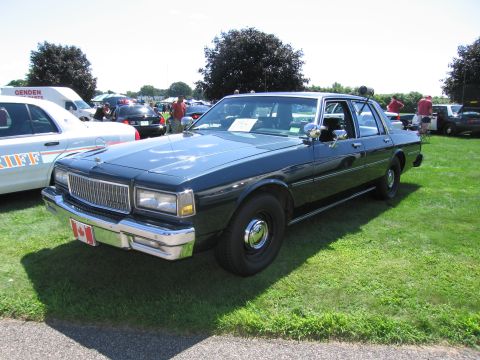 1991 Ford LTD Crown Victoria - dark 1980s Chevrolet Caprice sedan with a Canadian flag front plate parked on grass among other show cars.