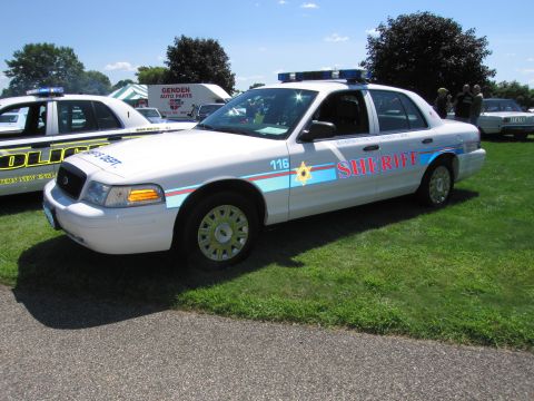 1991 Ford LTD Crown Victoria - white Ford Crown Victoria sheriff cruiser marked SHERIFF and unit 116 with a roof lightbar at an outdoor police-car show.