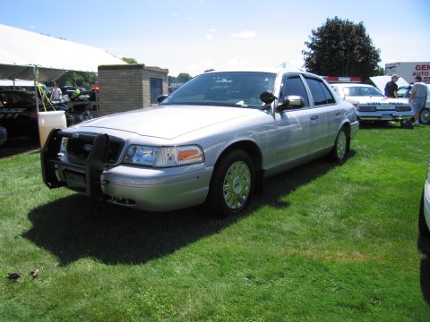 1991 Ford LTD Crown Victoria - silver Ford Crown Victoria sedan with a front push bar and spoke wheels parked on grass at an outdoor show.
