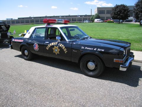 1991 Ford LTD Crown Victoria - black and white Dodge highway patrol sedan lettered HIGHWAY PATROL and To Protect & Serve with a red roof beacon.