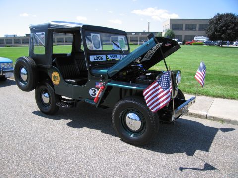 1991 Ford LTD Crown Victoria - dark green vintage Willys-style Jeep with the hood raised, soft top, and small American flags on the front bumper.