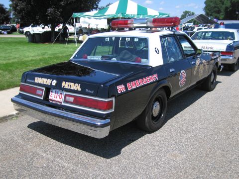 1991 Ford LTD Crown Victoria - Rear view of a black and white Dodge highway patrol sedan lettered HIGHWAY PATROL and 911 EMERGENCY with roof lightbar.