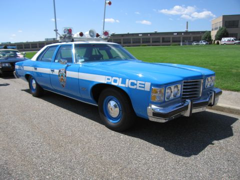 1991 Ford LTD Crown Victoria - blue and white 1970s Pontiac POLICE sedan with NYPD-style markings and multiple roof beacons parked on pavement.